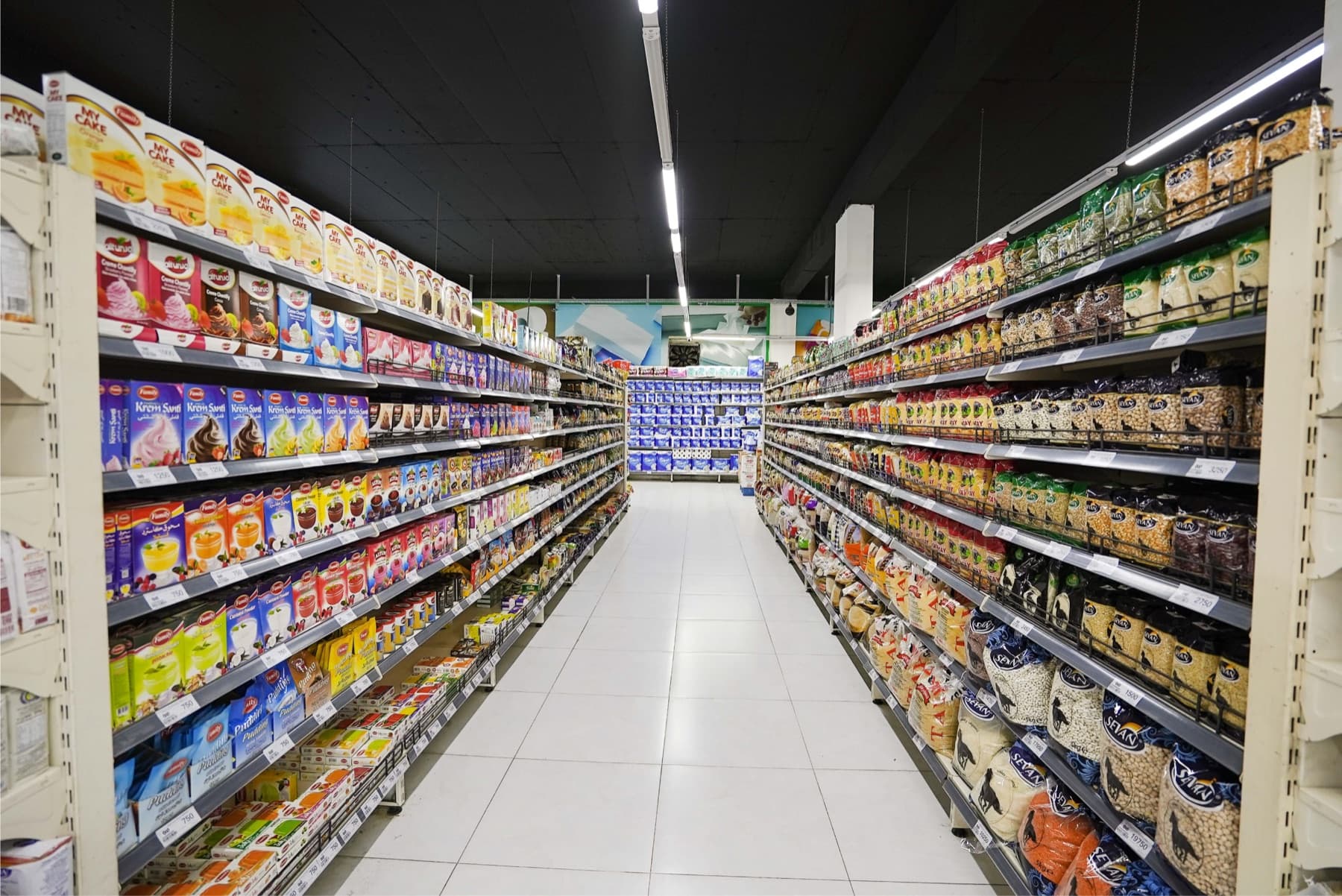 Wide Iraqi supermarket aisle with competing packaged-food brands across both shelves